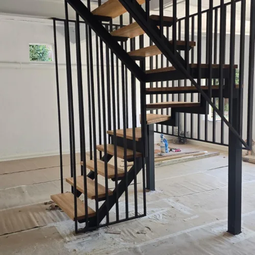 Escalera metálica de zanca central con meseta intermedia y peldaños de roble