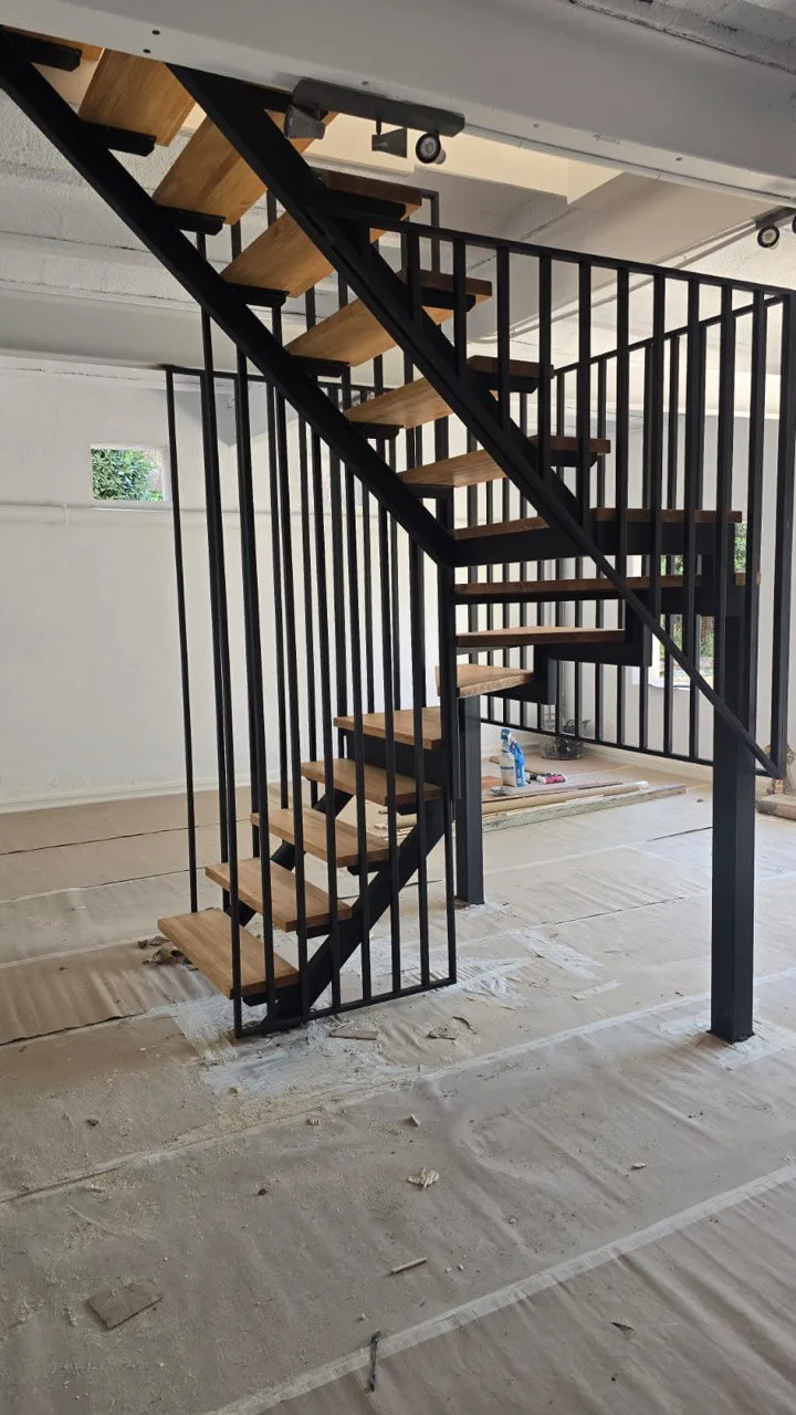 Escalera metálica de zanca central con meseta intermedia y peldaños de roble